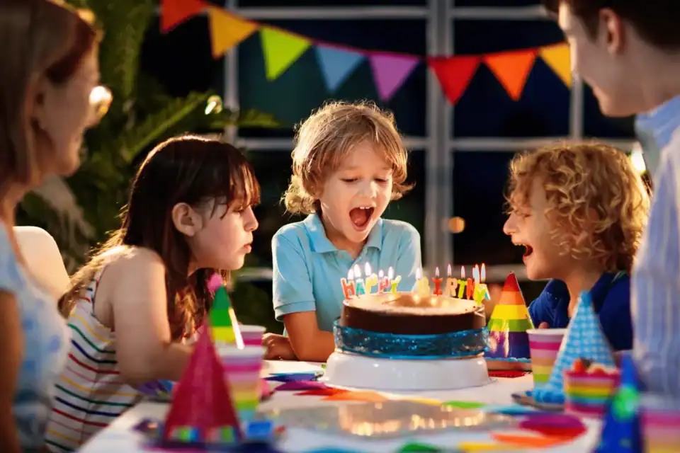Boy blowing out the candles on his birthday cake with his friends and family around