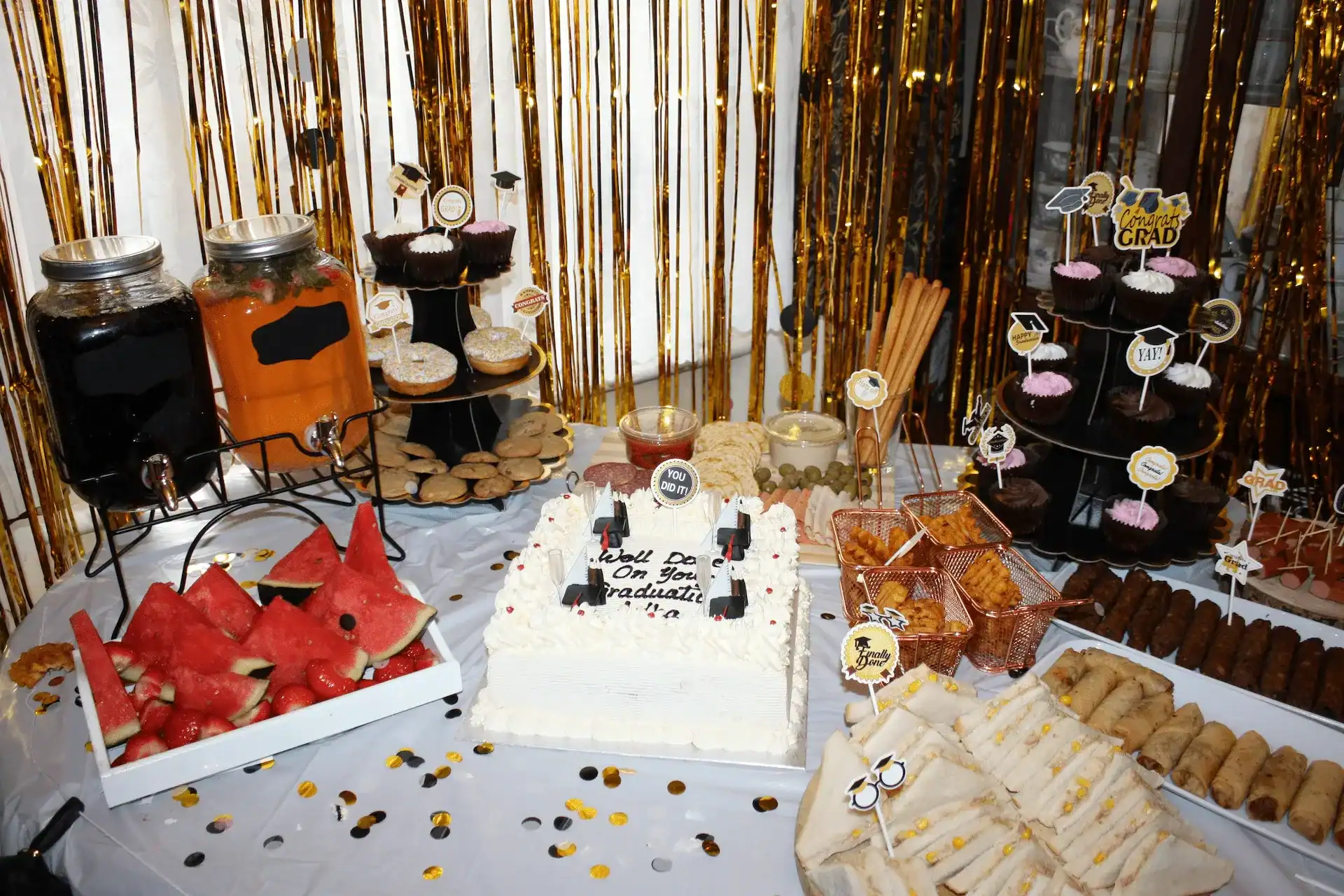 Graduation party decor and treats table with lots of cookies and other food and desserts